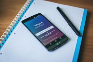 Instagram on a phone beside a notebook on a marketing desk